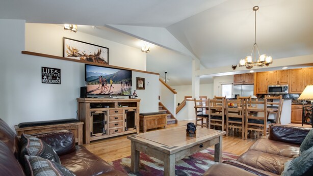 Amplia sala de estar con televisor grande, mobiliario de madera y una escalera que conduce al piso superior.