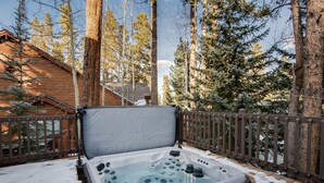 Un jacuzzi en un muelle cubierto de nieve, con una valla de madera y altos árboles al fondo.