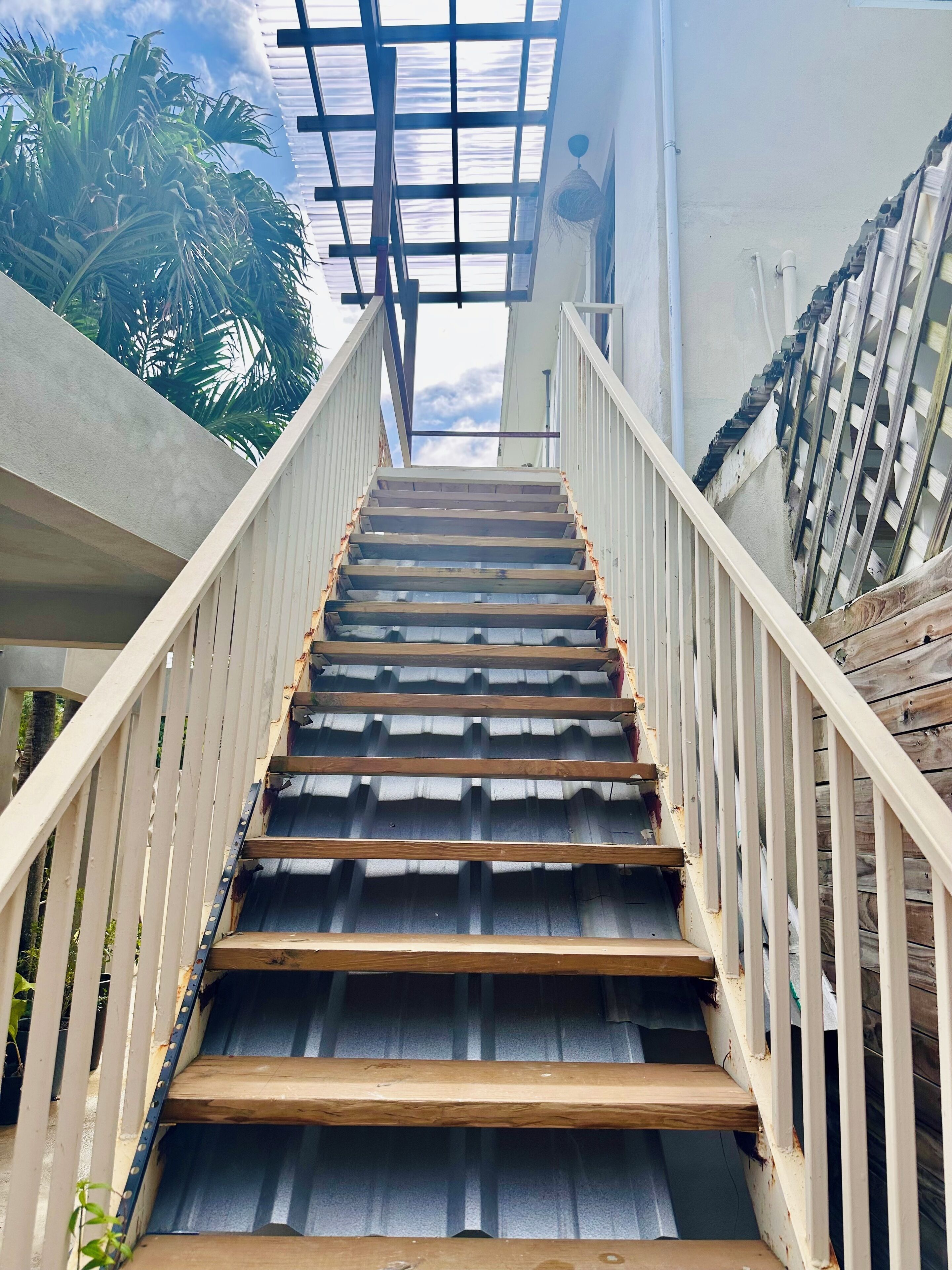 A staircase with wooden steps and white railings, leading up to a covered area with a metal roof.