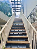 A staircase with wooden steps and white railings, leading up to a covered area with a metal roof.