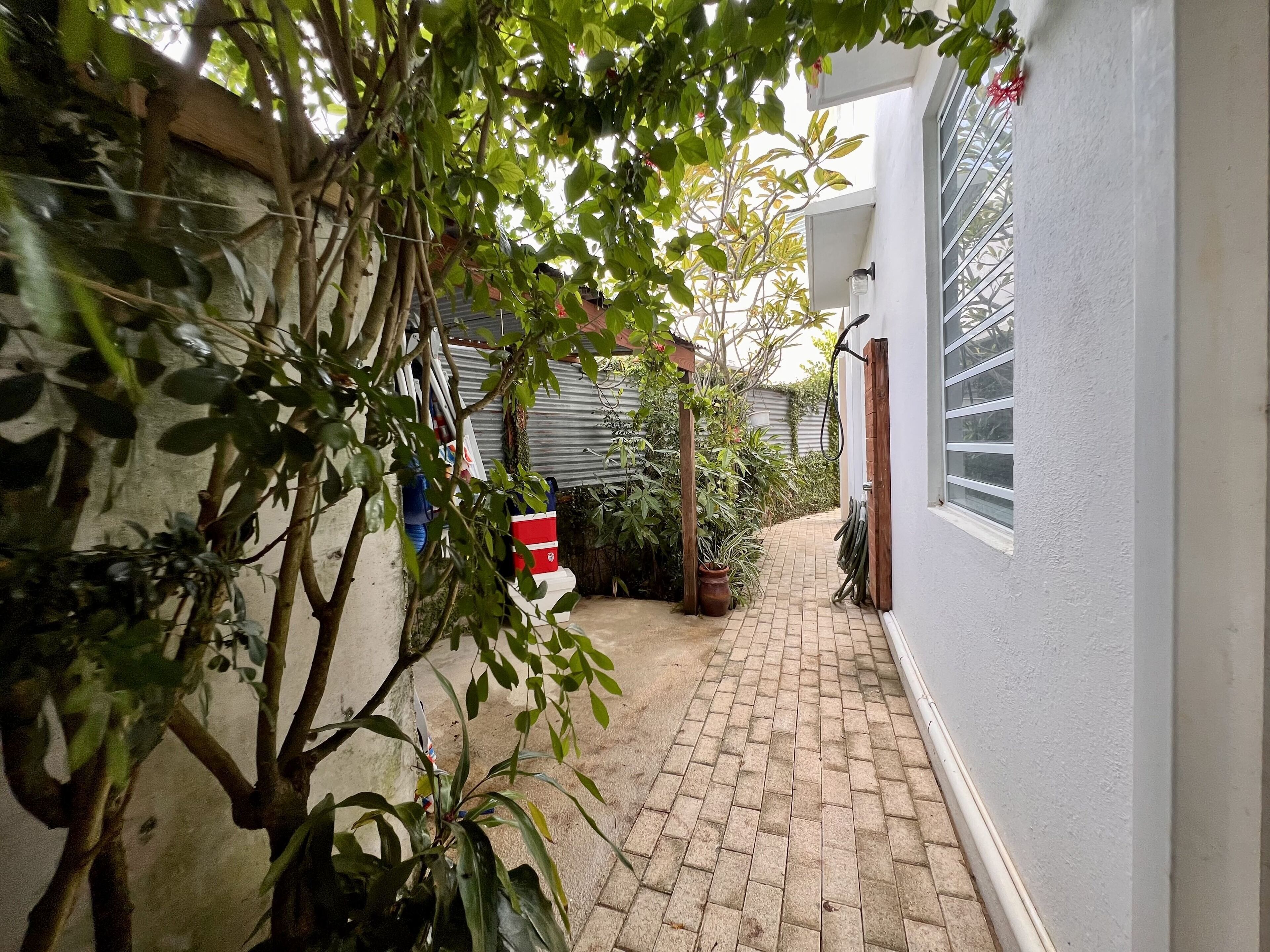 A narrow brick pathway leading to a white building with a window.