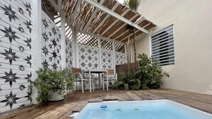 A pool area with a wooden deck, a table and chairs, and a pergola with a lattice design. - Sonsoleá Host (Luquillo)