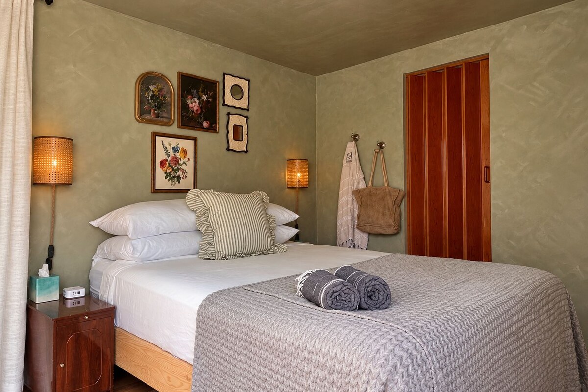 A bedroom with a bed, bedside lamps, a wooden nightstand, a wardrobe, and wall-mounted artwork.