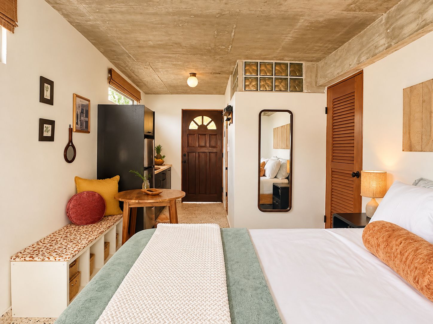 Un dormitorio con cama, mesita de noche, espejo y vista al pasillo.