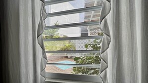 A window with a view of a swimming pool and greenery outside. - Sonsoleá Host (Luquillo)