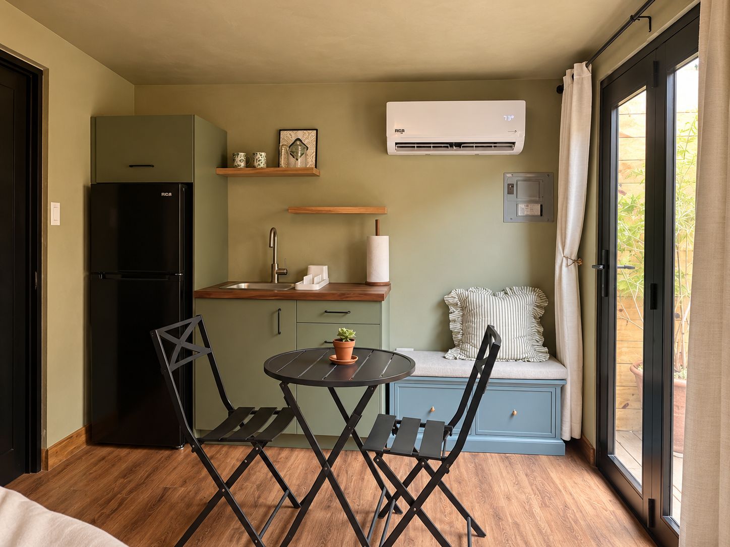 Una kitchenette compacta con refrigerador, pileta y un pequeño comedor con mesa y sillas.