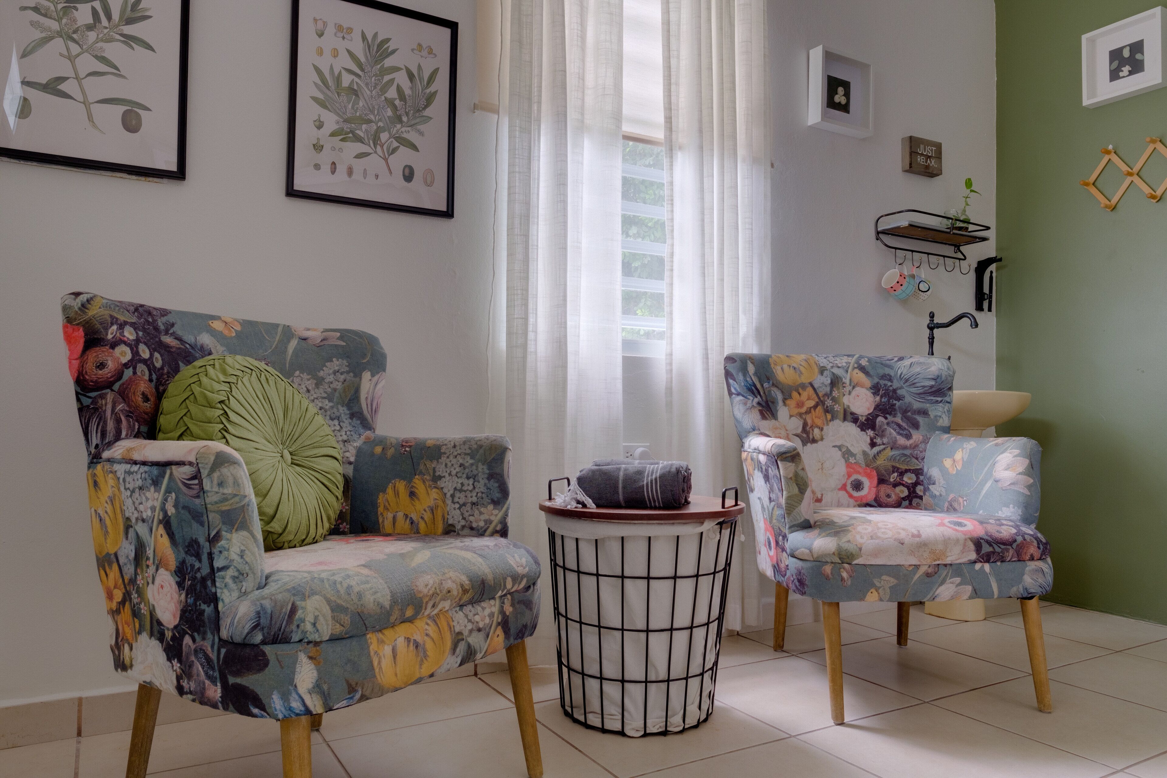 A room with two floral-patterned armchairs, a small round table, and a window with sheer curtains.