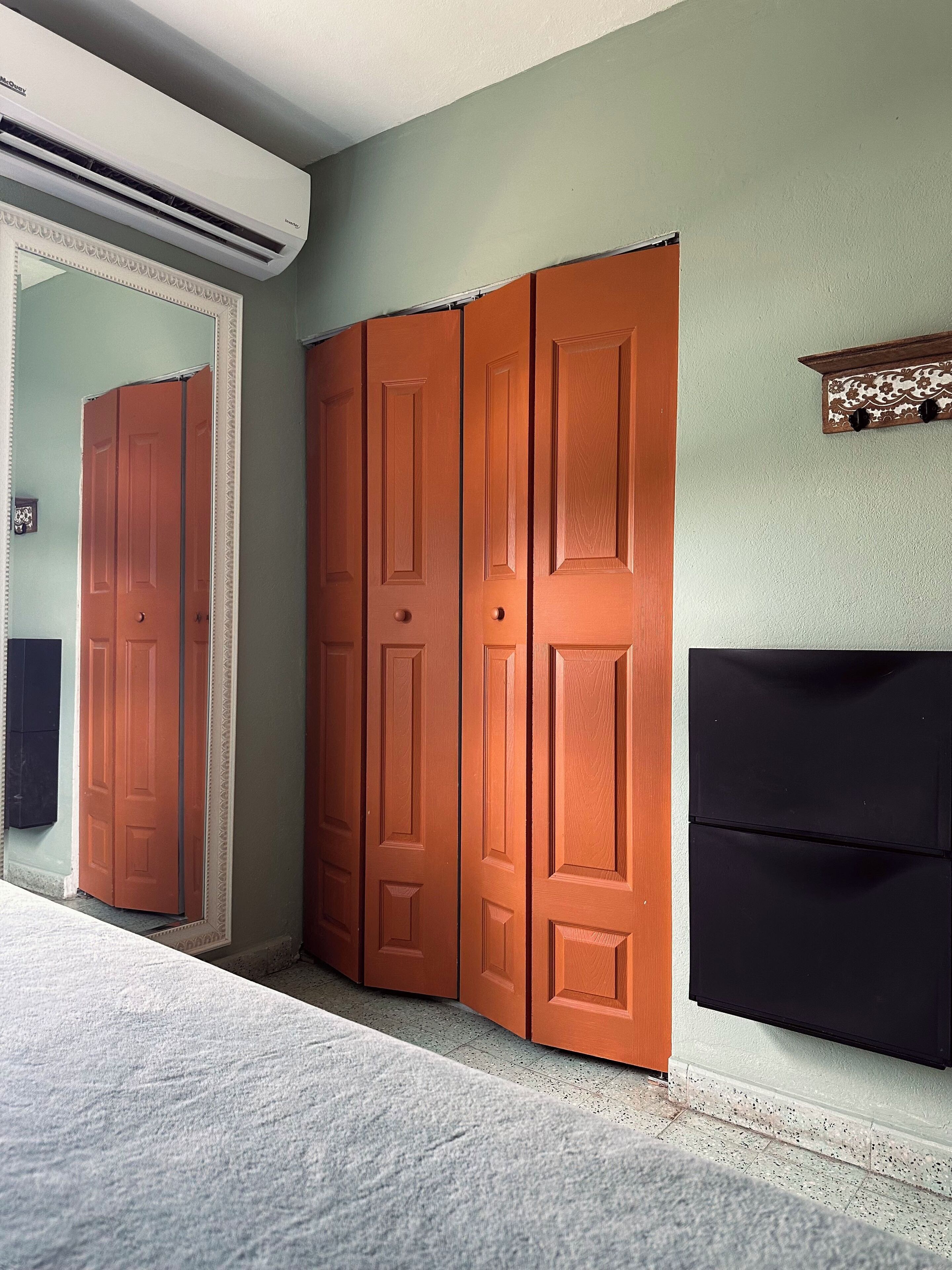 Una habitación con una puerta cerrada, aire acondicionado instalado en la pared y un armario negro.