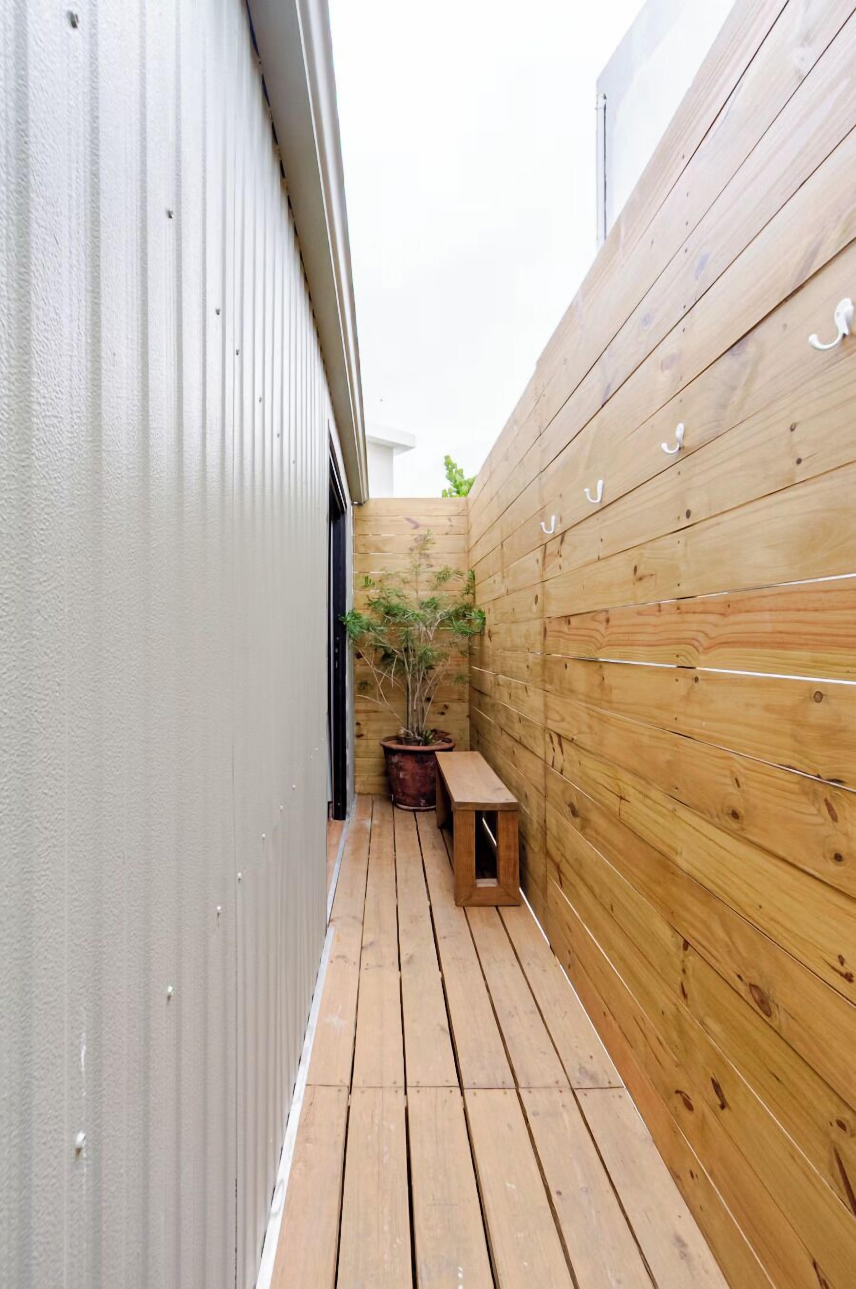 A narrow wooden deck with a bench and a potted plant.
