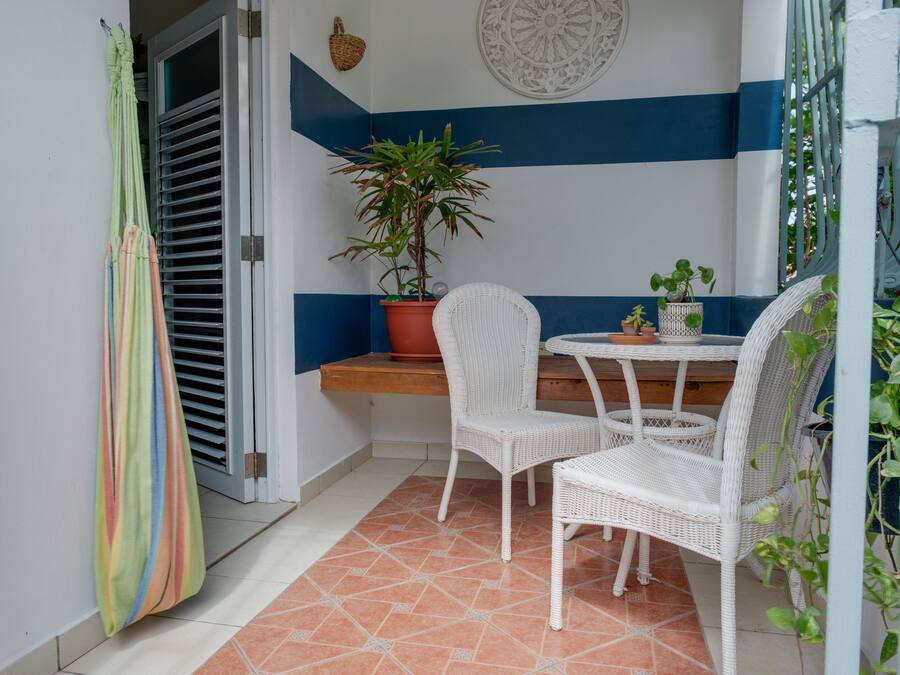 A small patio area with a white wicker table and chairs, a potted plant, and a striped curtain.