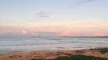 A beach with waves, a clear sky, and distant land.