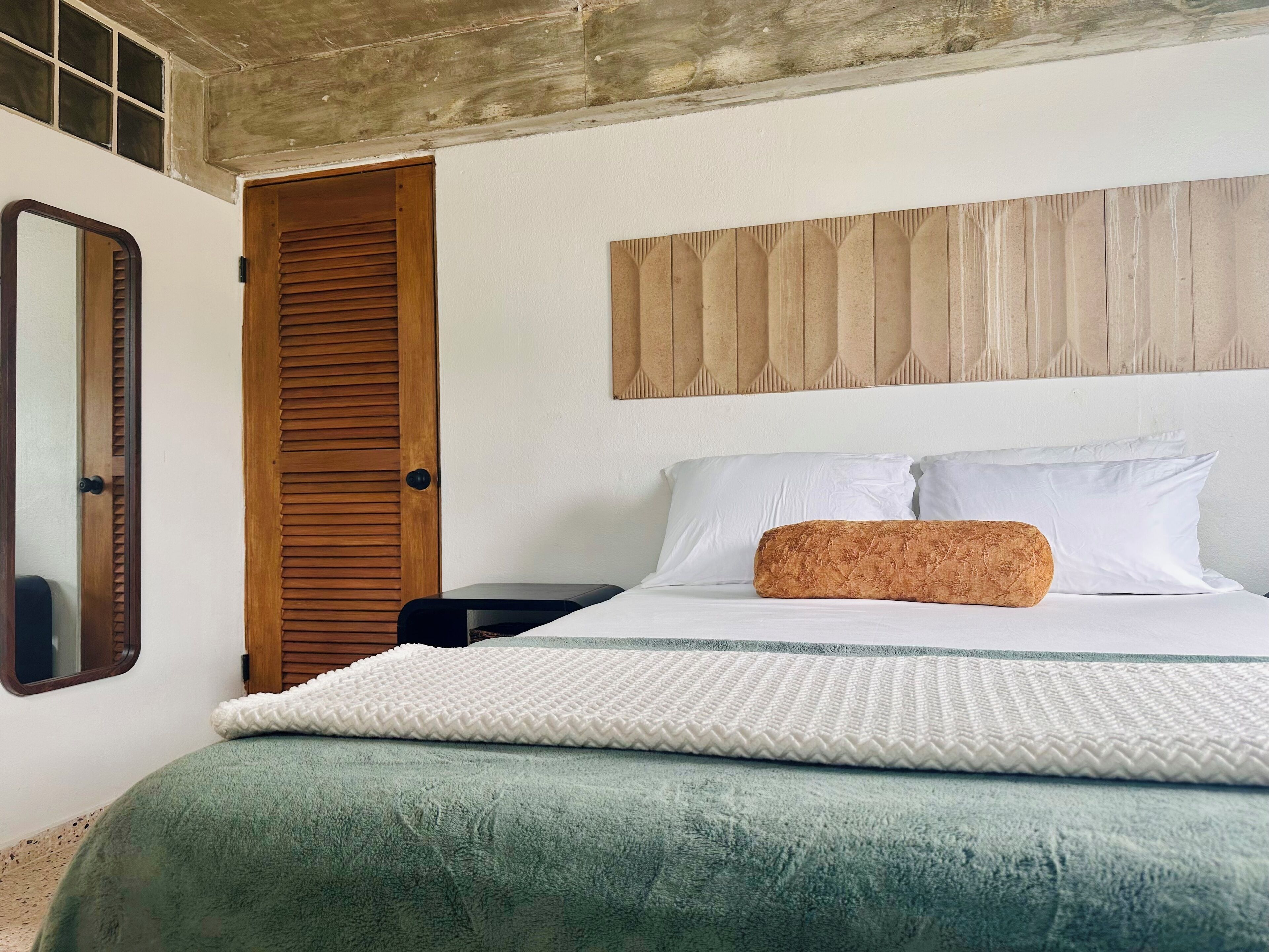 A bedroom with a bed, a wooden door, a nightstand, and a wall-mounted headboard.