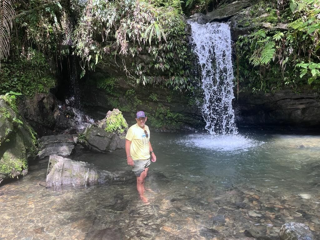 Eine Person steht in einem kühlen Pool, im Hintergrund ein Wasserfall.