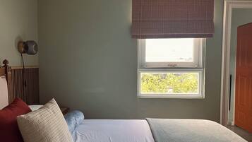 A bedroom with a bed, pillows, a radiator, a window with blinds, and an air conditioning unit.
