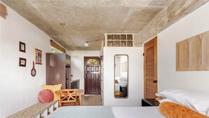A bedroom with a bed, a bench, a chair, a small table, a mirror, and a door leading to a bathroom. - Sonsoleá Host (Luquillo)