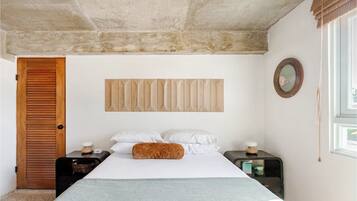 A bedroom with a bed, wooden headboard, bedside tables, a mirror, and a window.