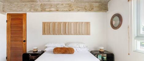 Un dormitorio con cama, cabecera de madera, mesitas de noche, un espejo y una ventana.