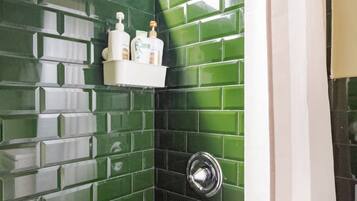 Un baño con paredes de azulejos verdes, un estante blanco con artículos de aseo y una cortina de ducha.