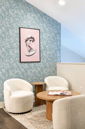 A modern living room with a patterned wallpaper, a framed artwork, and a round coffee table with a magazine.