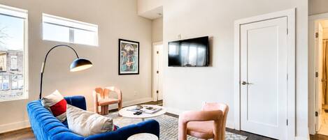 Ett modernt vardagsrum med en blå soffa, en rosa fåtölj, ett runt soffbord och en platt-TV som är monterad på väggen.