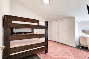 Un dormitorio con una cama de madera oscura, un armario blanco y un tapete estampado en tonos rosados.