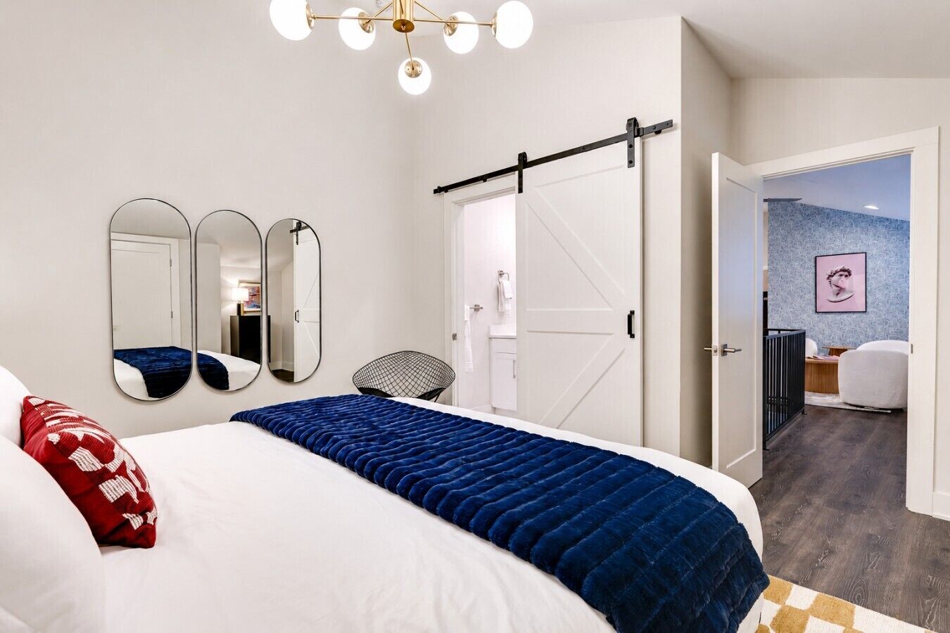 A modern bedroom with a bed, a large mirror, a wardrobe, and a door leading to a bathroom.