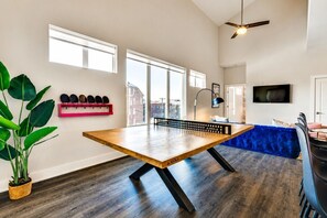 A ping pong table in a room with a city view, a blue sofa, and a TV on the wall.
