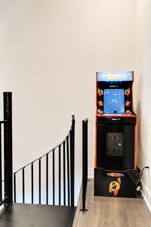 Een trap met een zwarte leuning en een retro speelautomaat met de tekst 'PACMAN' onderaan.