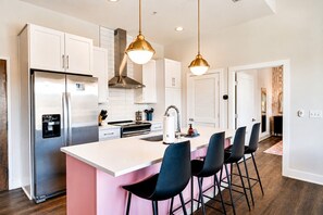 Una cocina moderna con electrodomésticos de acero inoxidable, una isla central con taburetes de bar, iluminación colgante y vistas al área de comedor.