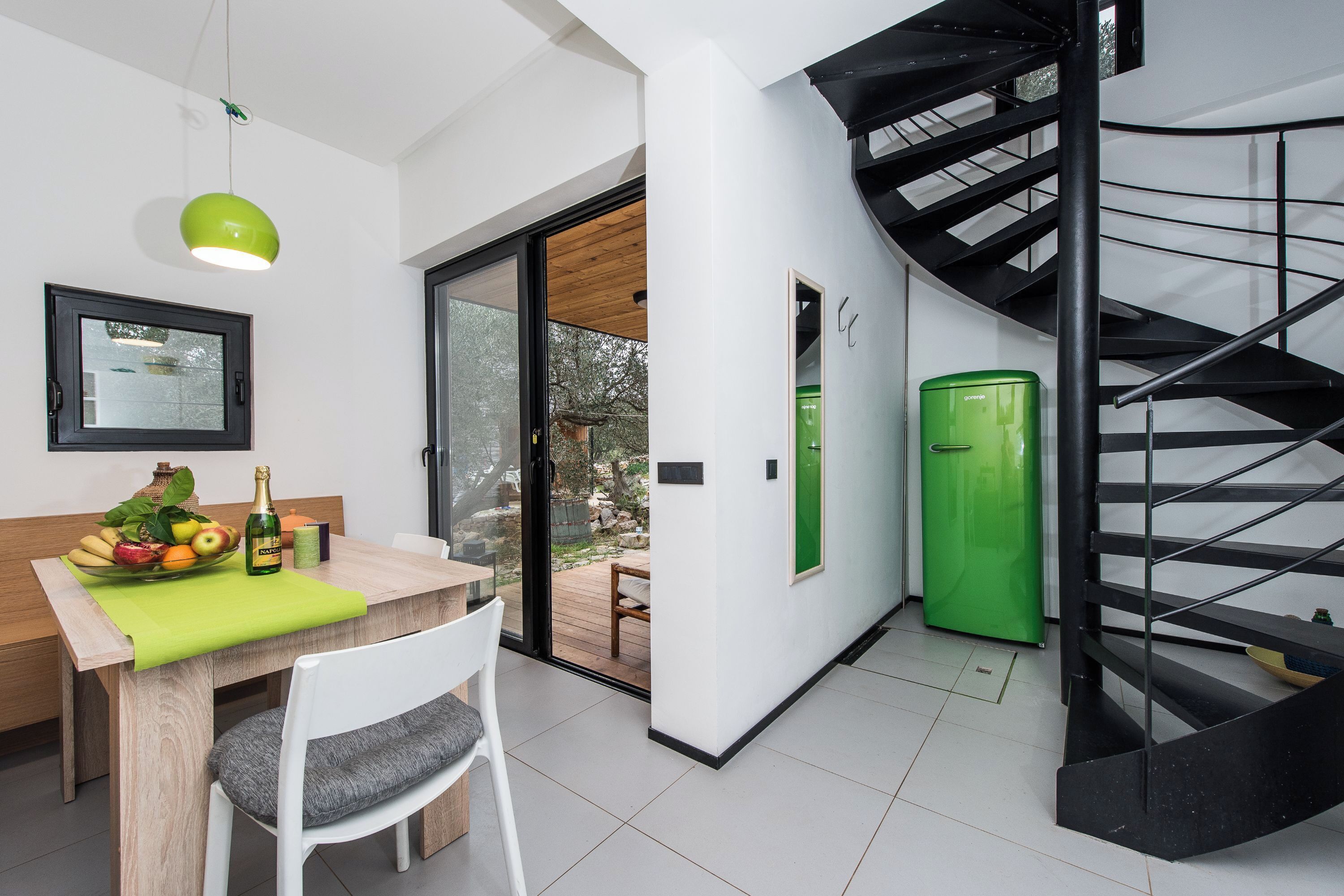 A modern kitchen with a dining table, a green pendant light, and a view of the outdoors.