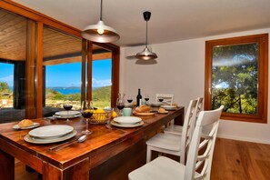 Un comedor con una mesa de madera dispuesta para una comida, vista al exterior y un ventanal grande.