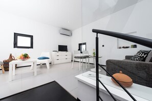 A modern, minimalist living space with a white sofa, a dining table, and a kitchen area.