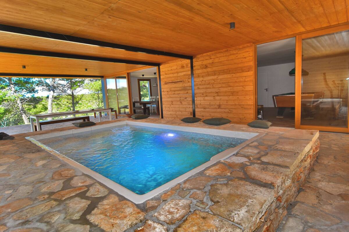 Piscina interior com piso de pedra, paredes de madeira e um banco.