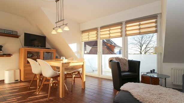 A modern living room with a dining area, large windows, and a cozy seating arrangement. - Ferienwohnung Oberdeck (Norden)