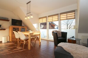 A modern living room with a dining area, large windows, and a cozy seating arrangement. - Ferienwohnung Oberdeck (Norden)