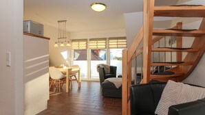 A modern living space with a dining area, a staircase, and a sofa. - Ferienwohnung Oberdeck (Norden)