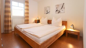 A double bed with a wooden frame, two bedside tables with lamps, and a window with curtains. - Ferienwohnung Oberdeck (Norden)