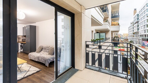 Ein modernes Apartment mit Balkon, Sofa, Küche und einer Glastür, die zu einem Stadtblick führt.
