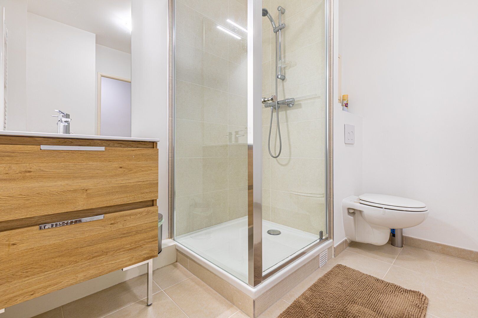 Een moderne badkamer met een douche in een glazen cabine, een houten wastafelmeubel en een wit toilet.