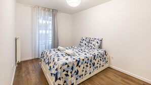 Ein Schlafzimmer mit Bett, Heizkörper, einem fenster mit Vorhängen und einer Deckenleuchte.
