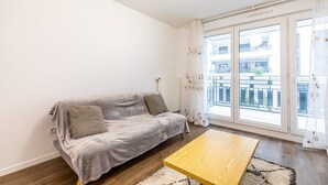 Ein modernes Wohnzimmer mit grauem Sofa, einem Holztisch und Blick auf einen Balkon mit Geländer.