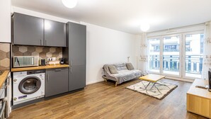 Eine moderne Wohnung mit Küche, Waschmaschine, grauem Sofa und einem Balkon mit Blick.