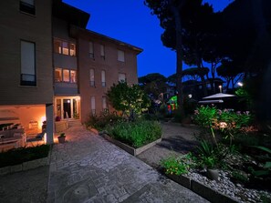 A courtyard with a stone pathway, a small seating area, and a building with multiple windows. - Casa Pineta (Grosseto)