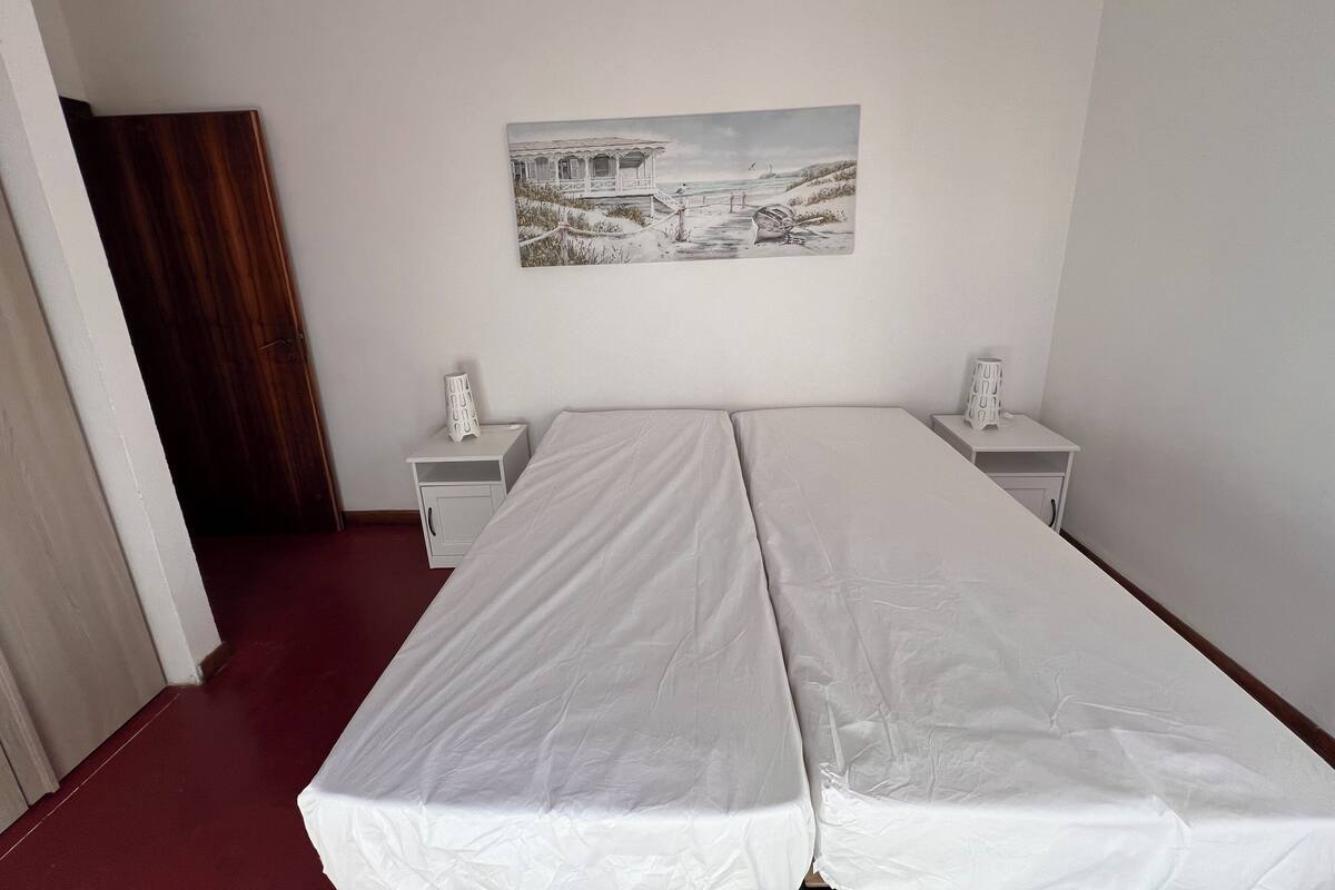 A room with a bed, a nightstand, a wall-mounted picture, and a door.