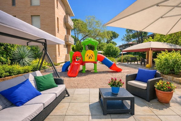 A patio area with outdoor seating, a children's play structure, and a building in the background.
