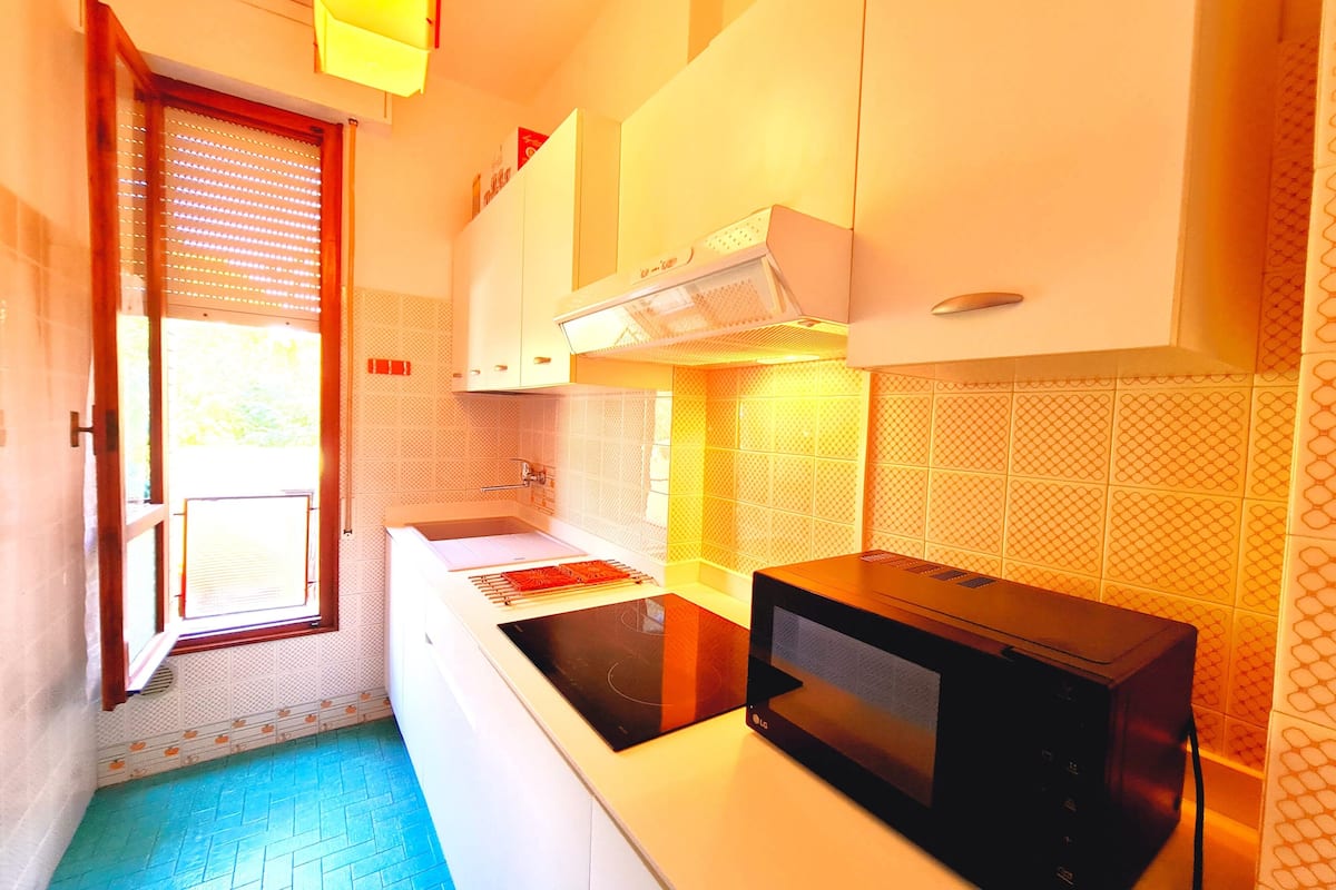 A compact kitchen with a microwave, stove, and a window with blinds.