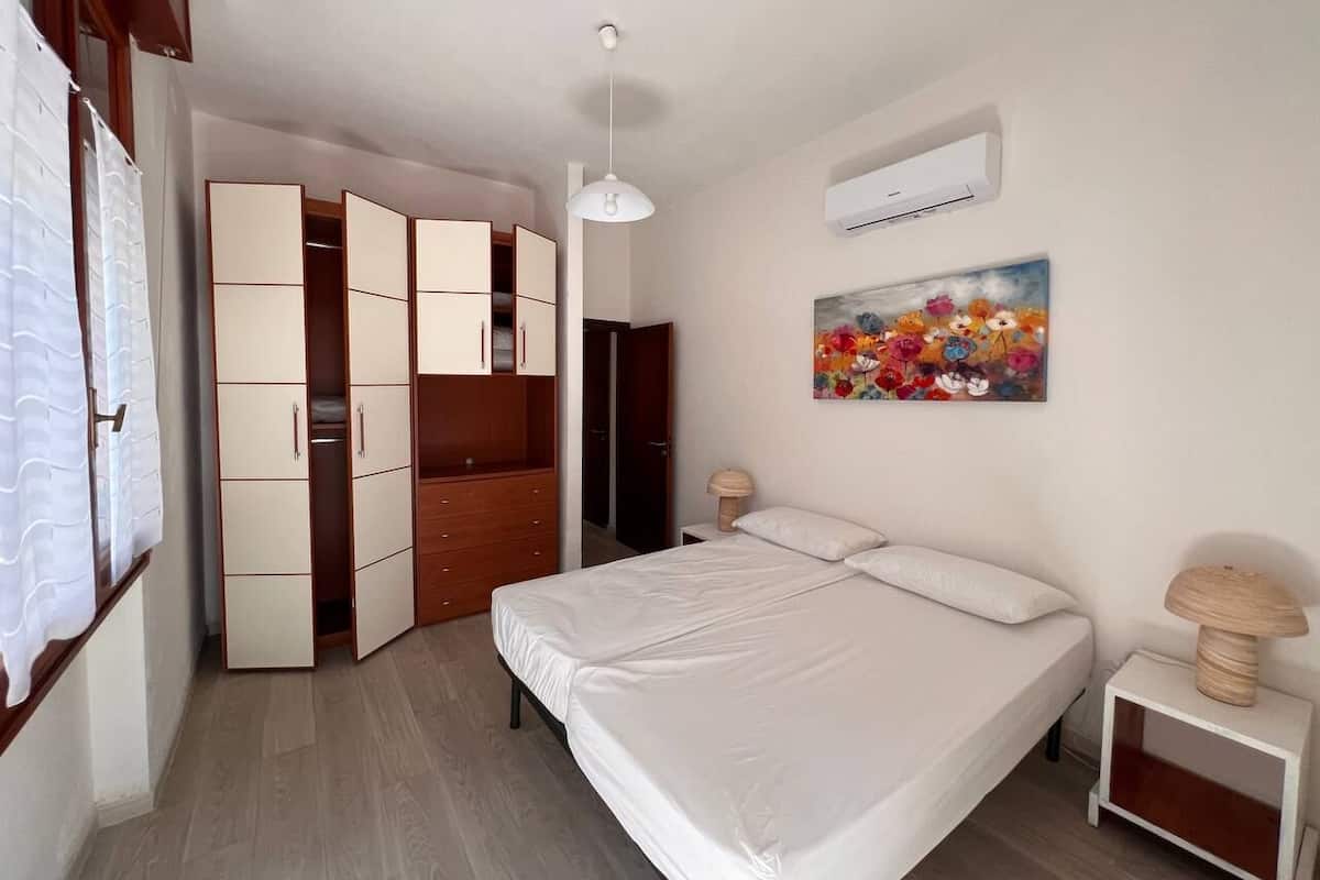 A bedroom with a bed, a wardrobe, a painting, and a nightstand.