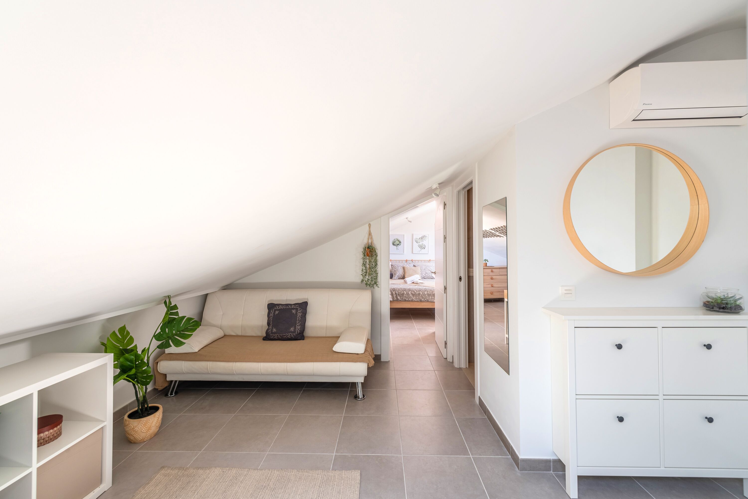 A modern, well-lit room with a sofa, a round mirror, and a white dresser.