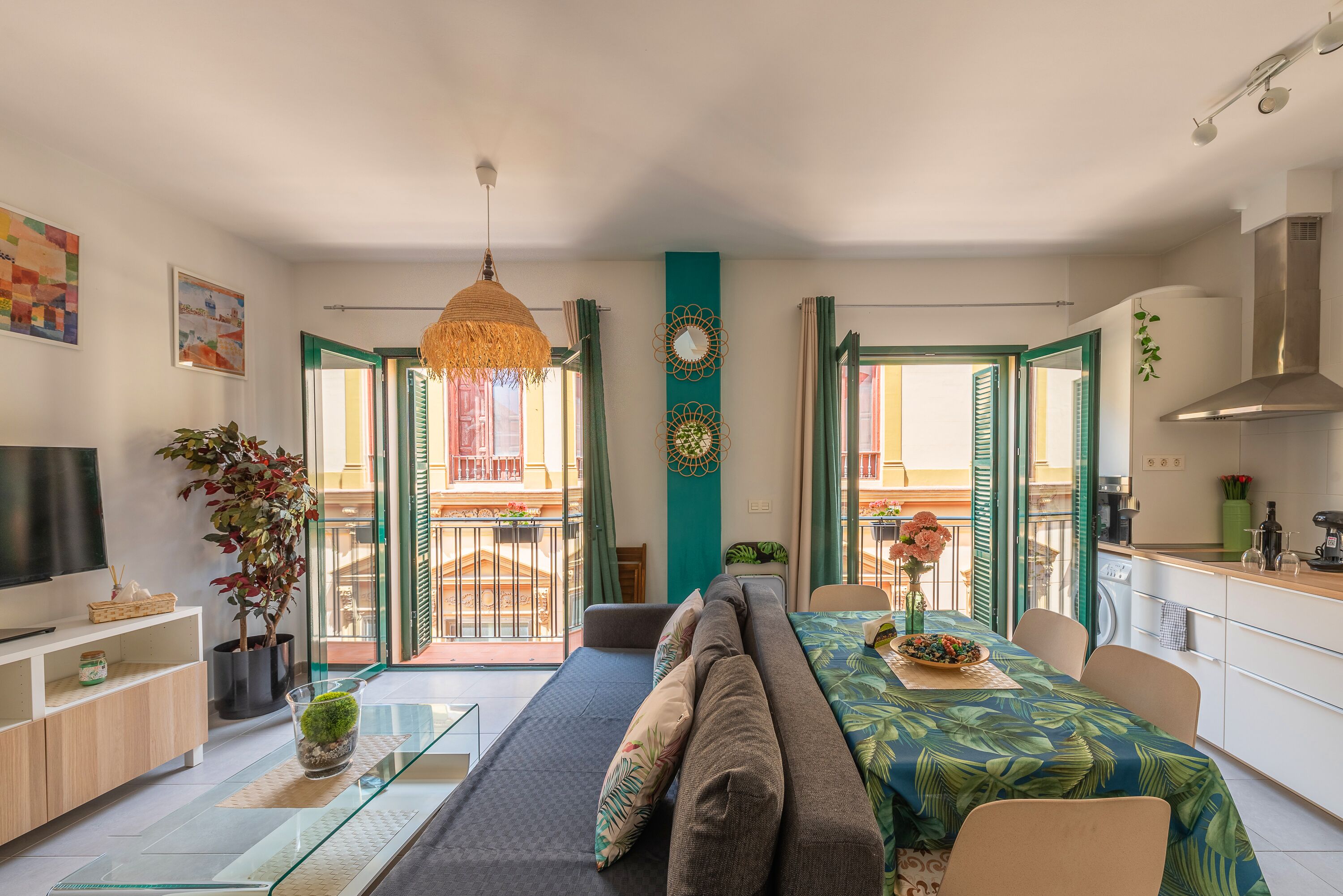 Een moderne woonkamer met een bank, een glazen salontafel en een televisie. Er is een balkon met uitzicht op de stad.