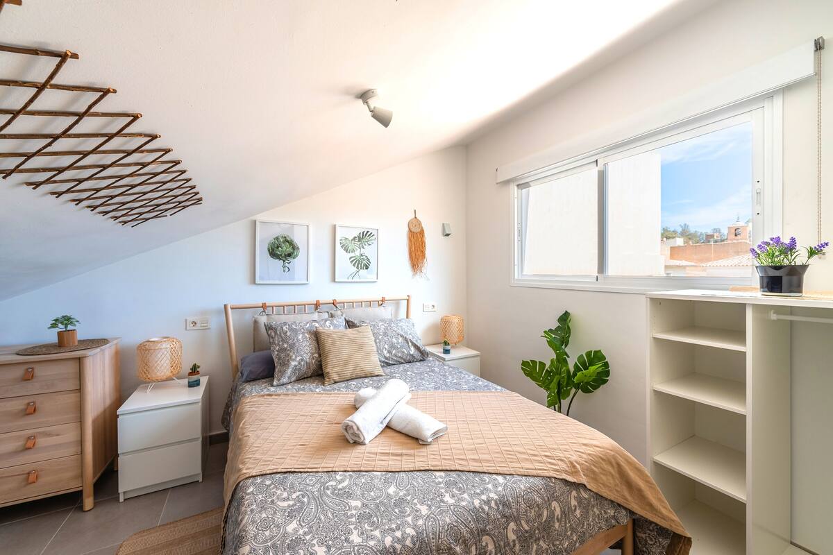 Quarto com cama, mesas de cabeceira, janela e um varal.